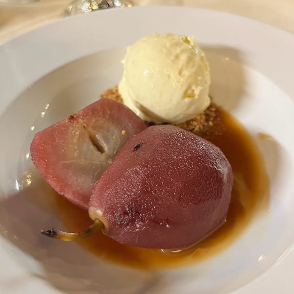 Poached pears in syrup with a scoop of vanilla ice cream and crumble on a white plate.