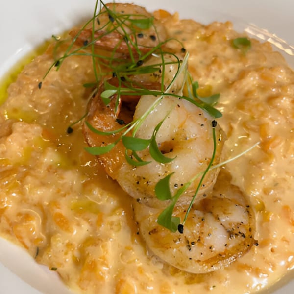 Creamy orange risotto topped with grilled shrimp, fresh herbs, and black pepper.