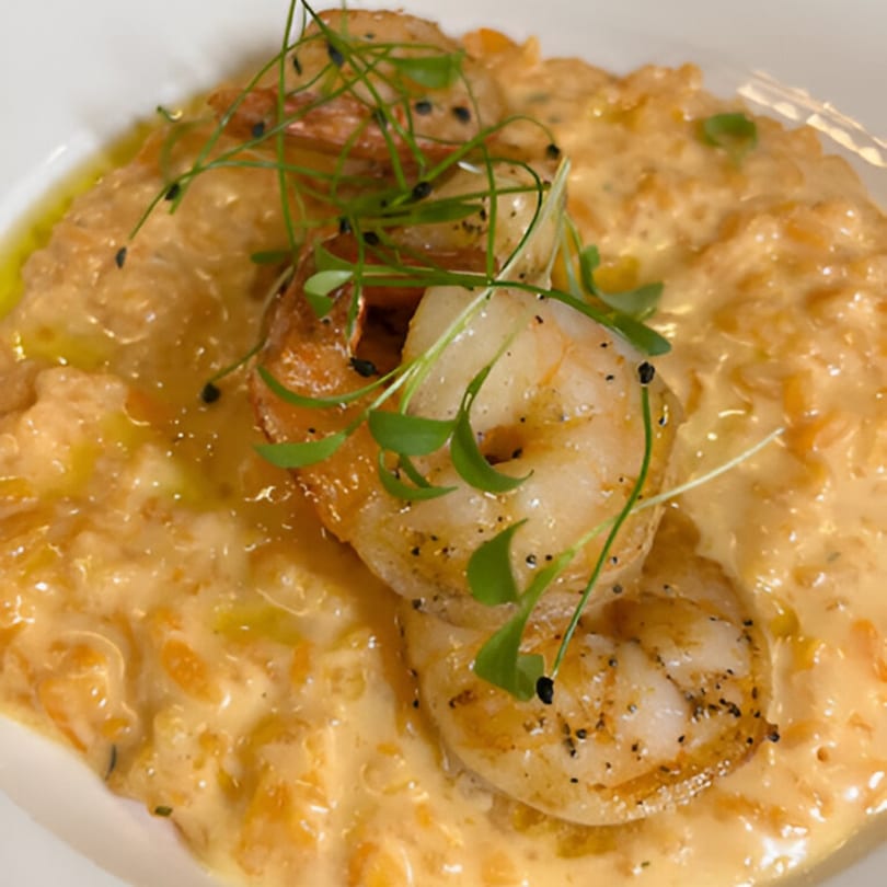 Creamy orange risotto topped with grilled shrimp, fresh herbs, and black pepper.