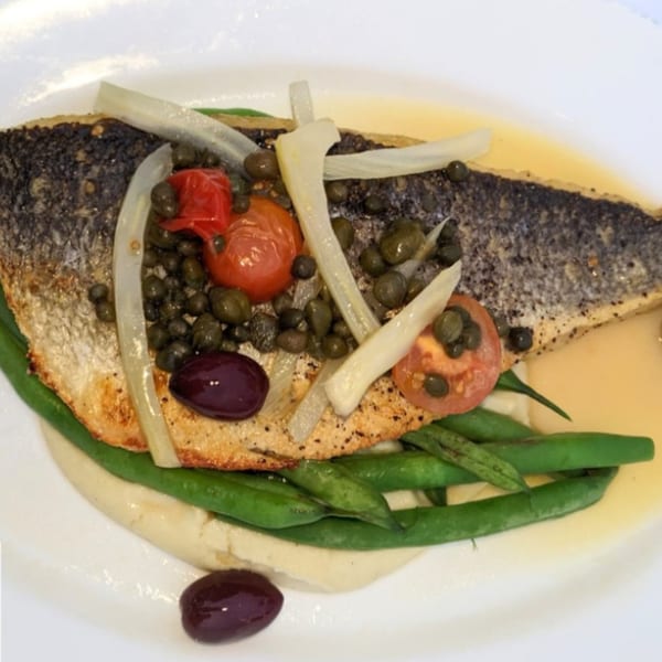 Sontuosa's pan-seared fish with crispy skin, green beans, tomatoes, capers, and olives on a white plate.