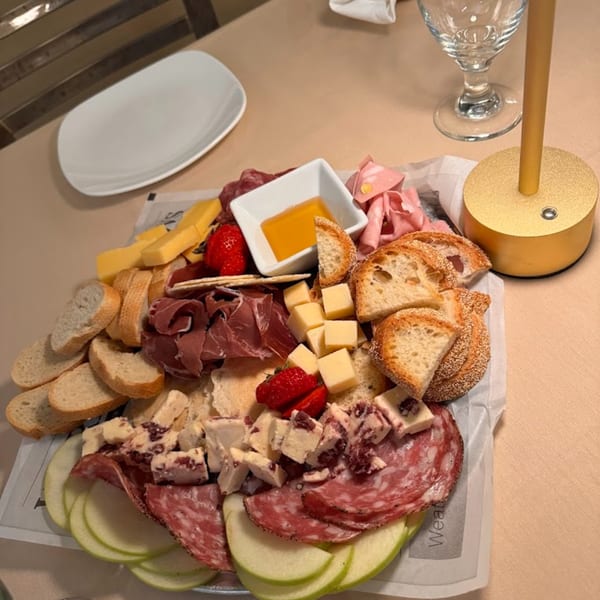 A Sontuosa charcuterie board with meats, cheeses, bread, fruit, and honey on a table.