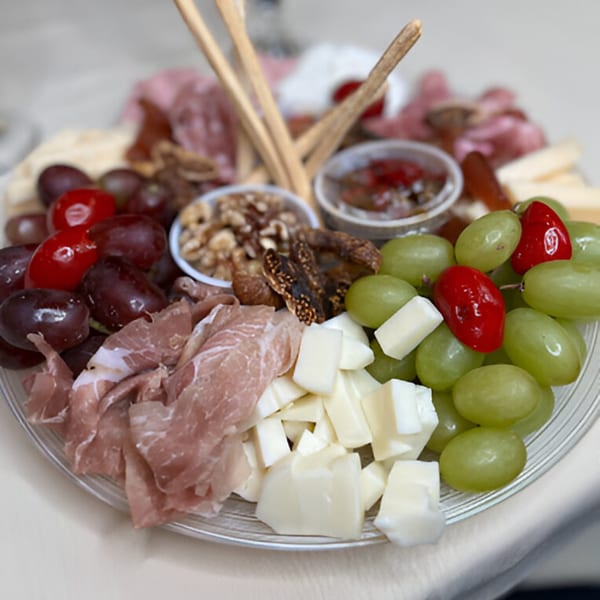 A Sontuosa charcuterie board with prosciutto, cheeses, grapes, nuts, dried figs, and breadsticks.